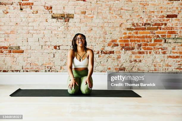 wide shot portrait of laughing woman kneeling in yoga studio after class - hand on knee fotografías e imágenes de stock