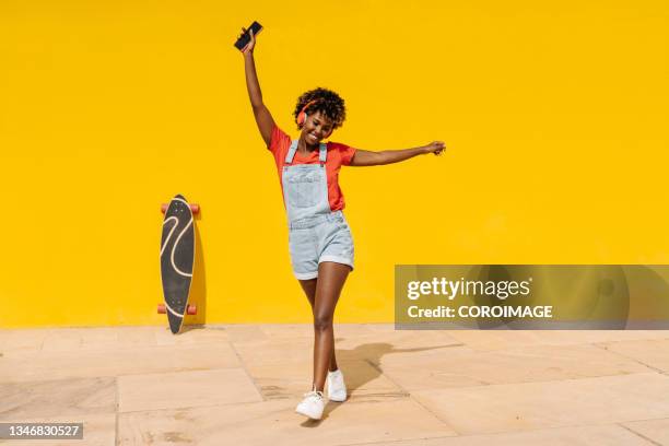 positive and excited afro woman dancing while listening music with headphones outdoors. - woman headphones sport smile iphone stock pictures, royalty-free photos & images