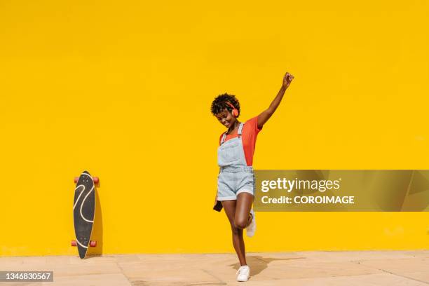 cheerful afro skater woman dancing while listening to music with headphones outdoors. - woman headphones sport smile iphone stock pictures, royalty-free photos & images