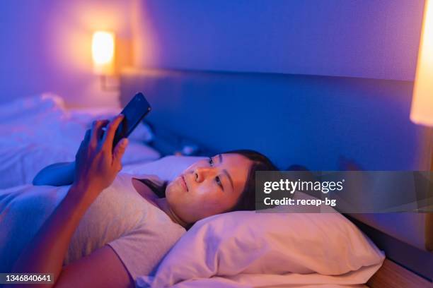 young woman using smart phone in bed at night at home - midnight stock pictures, royalty-free photos & images