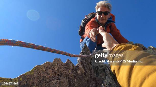 mountaineer offers woman a hand up mountain peak - 爬山繩 個照片及圖片檔