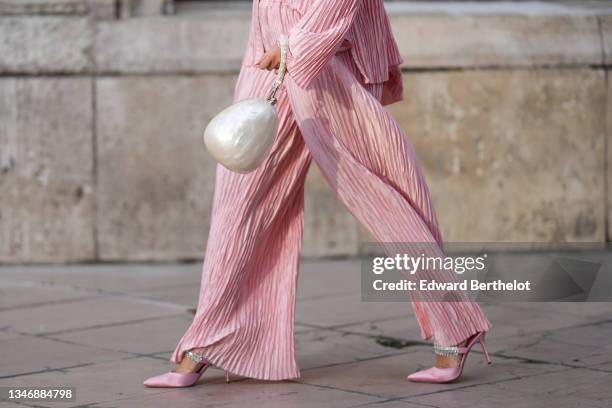 Katie Giorgadze wears pleated pink pyjama trousers from J’amemme, a pleat pink pajama shirt from J’amemme, an ivory egg pearl embellished oval shaped...