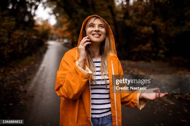 smiling young woman in yellow raincoat taking on a smart phone in rainy day - impermeável repelente de água imagens e fotografias de stock