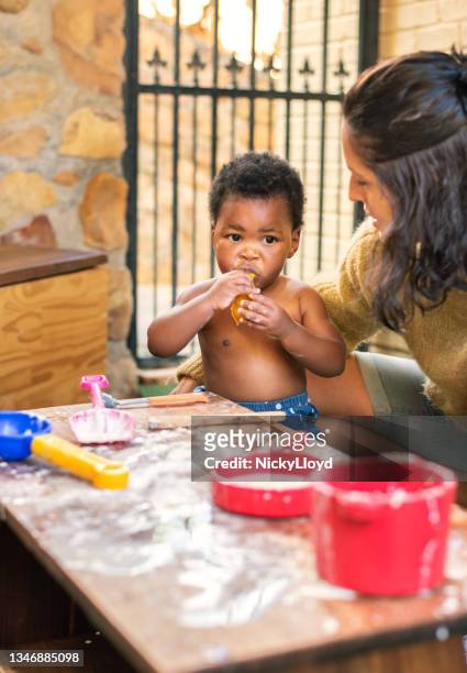 mama sitzt mit ihrem kleinen mädchen, während sie zusammen an einem tisch draußen spielt - baby spielt mit essen stock-fotos und bilder