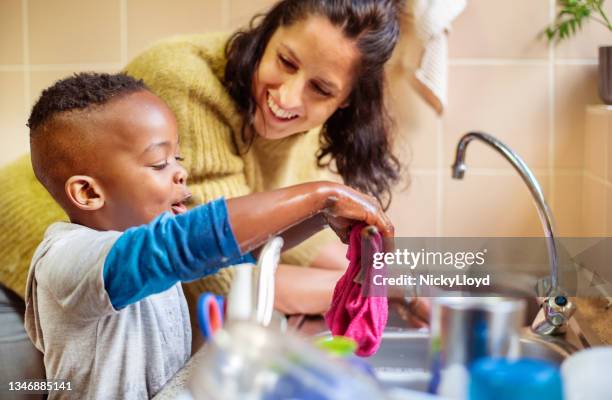 petit garçon souriant et sa mère lavant la vaisselle ensemble dans leur cuisine - adoption photos et images de collection