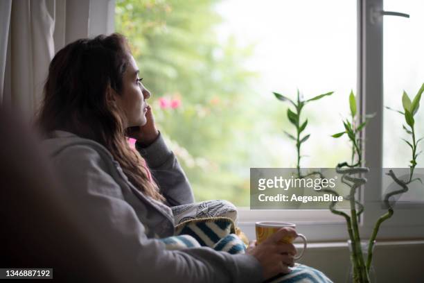 donna depressa seduta alla finestra - tristezza foto e immagini stock
