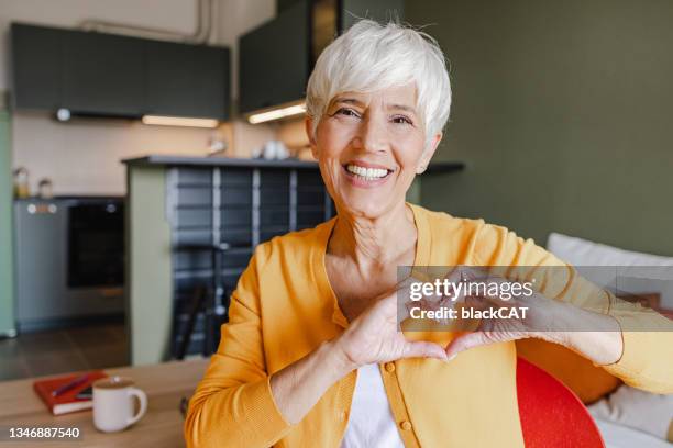 portrait of a senior woman at home showing a heart-shaped symbol - heart health 個照片及圖片檔