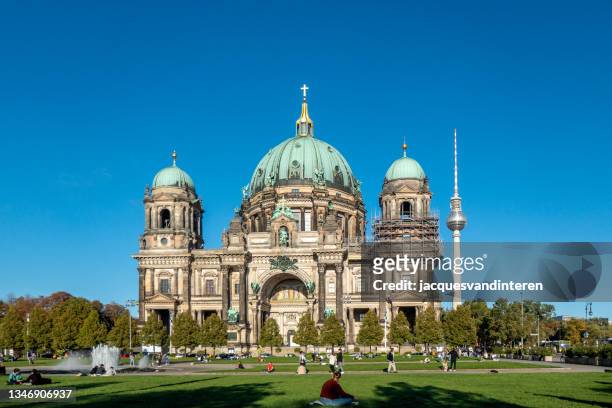 berlin cathedral (germany) with the television tower on alexander platz in the background. in front of the church people sit in the grass in the sun - berlin cathedral stock pictures, royalty-free photos & images