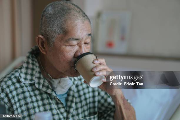 asian chinese senior male patient drinking coffee in hospital ward sitting on bed - traqueotomia equipamento cirúrgico imagens e fotografias de stock