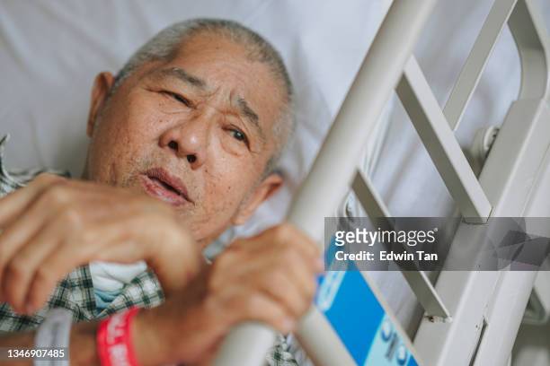 asiatischer chinesischer älterer männlicher patient mit schmerzen, der auf dem bett auf der krankenhausstation liegt und sich ausruht - adult male hospital bed stock-fotos und bilder