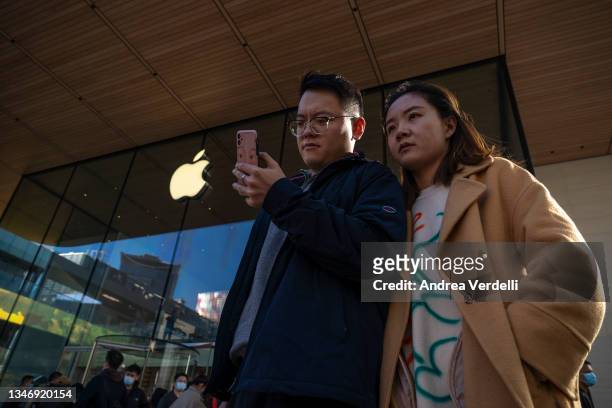 People watch a phone in front of an Apple store on October 16, 2021 in Beijing, China. According to an action plan released on October 14, Beijing...