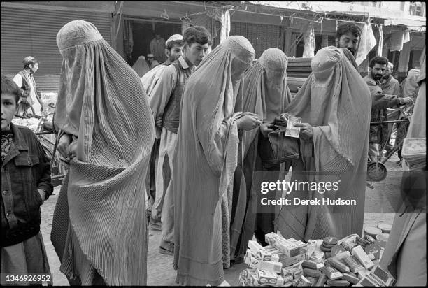 Group of women, all dressed in burkas, shop from cosmetics at an open-air stall, Kabul, Kabul Province, Afghanistan, October 2001. Several men watch...