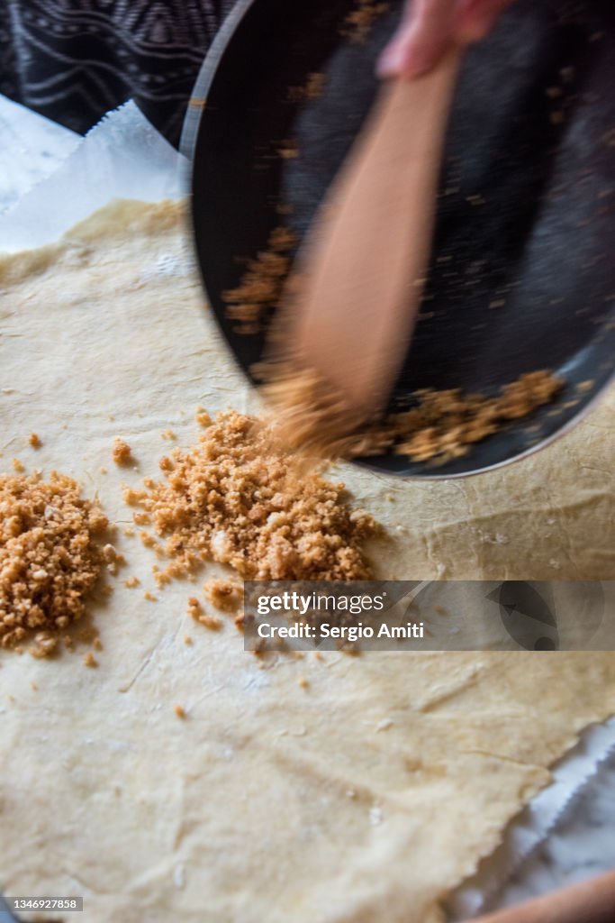 Adding toasted crushed amaretto biscuits from a pan onto rolled out dough