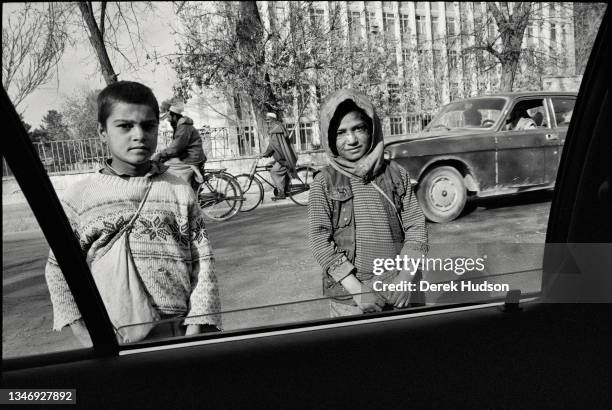 View, out of the open window of a car, of two children who beg for money at the side of a road, Kabul, Kabul Province, Afghanistan, October 2001.