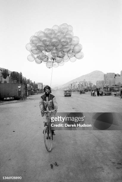 Smiling balloon seller bicycles along a road on the outskirts of Kabul, Kabul Province, Afghanistan, October 2001.