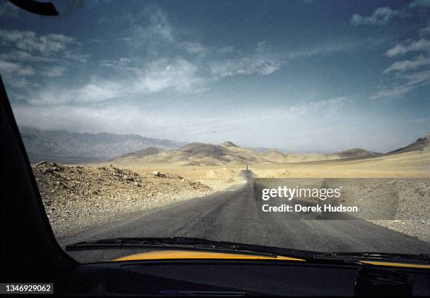 View of a tarmac road with distant mountains in the background seen through the windscreen of a taxi on the way to Panshir.