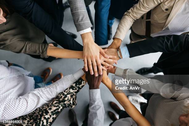 close-up of co-workers stacking their hands together - samenwerken stockfoto's en -beelden