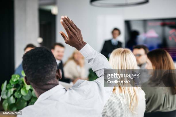 giovane uomo d'affari che alza la mano a una riunione - viso nascosto foto e immagini stock