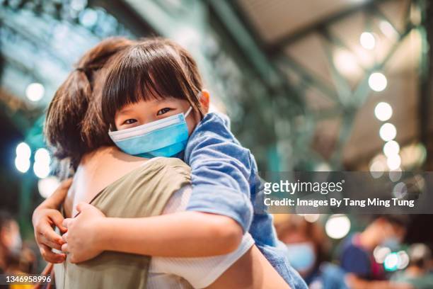 lovely little girl in protective face mask smiling joyfully at the camera  while her mom carrying her in the train station - china coronavirus ストックフォトと画像
