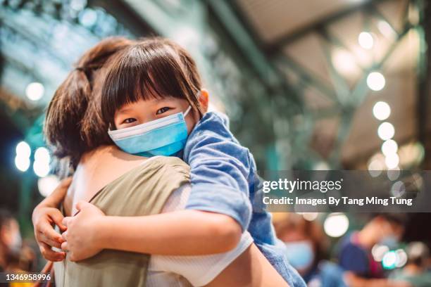 lovely little girl in protective face mask smiling joyfully at the camera  while her mom carrying her in the train station - covid 19 travel stock pictures, royalty-free photos & images