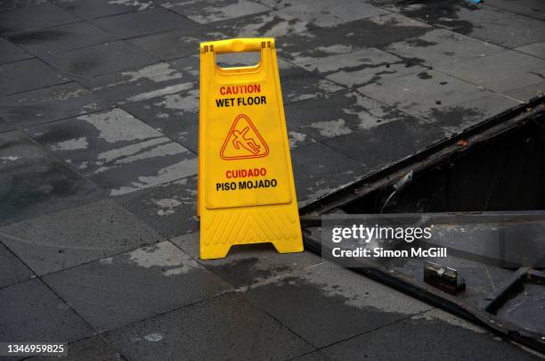 bilingual english/spanish 'caution wet floor/cuidado piso mojado' freestanding portable plastic warning sign on a sidewalk being cleaned - mojado stock-fotos und bilder