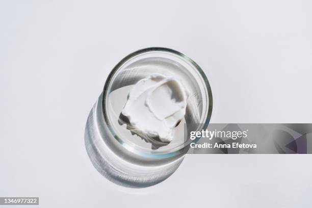 petri dish with a smear of white cream on gray background. concept of cosmetics laboratory researches. photography in flat lay style - lichaamsverzorging en schoonheid stockfoto's en -beelden