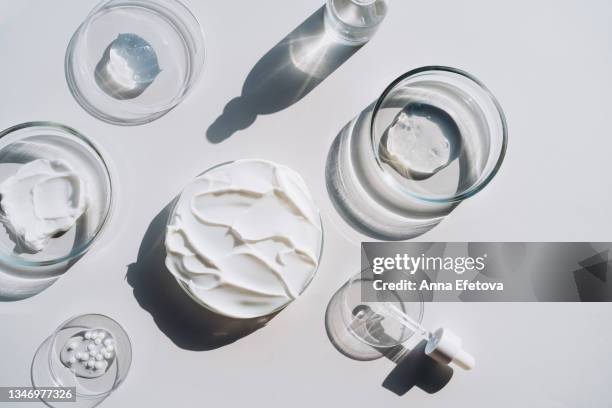 background made with many petri dishes with different cosmetics and a glass bottle with a face serum and a pipette on gray background. concept of cosmetics laboratory researches. photography in flat lay style - crèmekleurig stockfoto's en -beelden