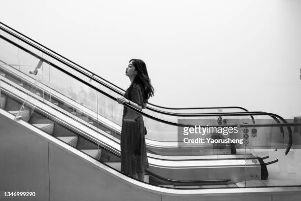 one asian woman taking the escalator - chinese young adults shopping imagens e fotografias de stock