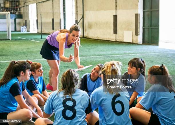 coach discussing game plan with girls soccer team - indoor football pitch stock pictures, royalty-free photos & images