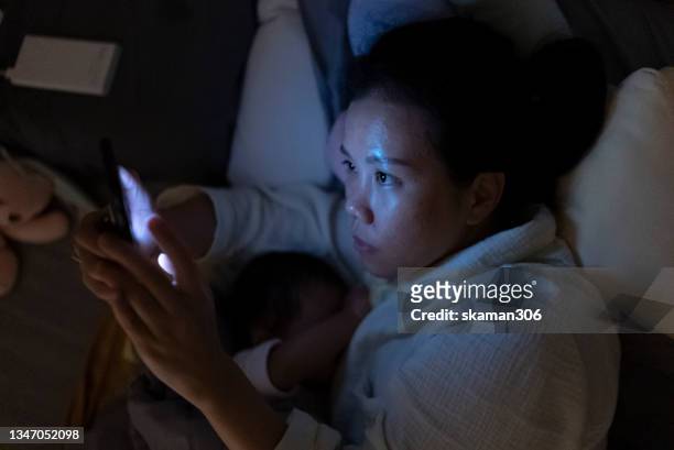 asian single mother positive emotion and breastfeeding her daughter late night and using phone  on the bed - baby depression stock-fotos und bilder