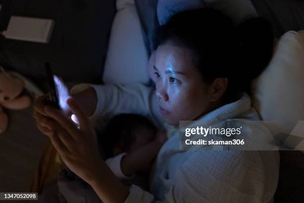 asian single mother positive emotion and breastfeeding her daughter late night and using phone on the bed - mom feeding baby at night stock pictures, royalty-free photos & images