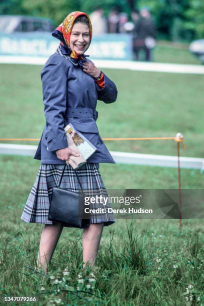 View of British monarch Queen Elizabeth II, in a silk headscarf, a blue coat, and a tartan skirt, as she smiles at the camera, Windsor, England,...