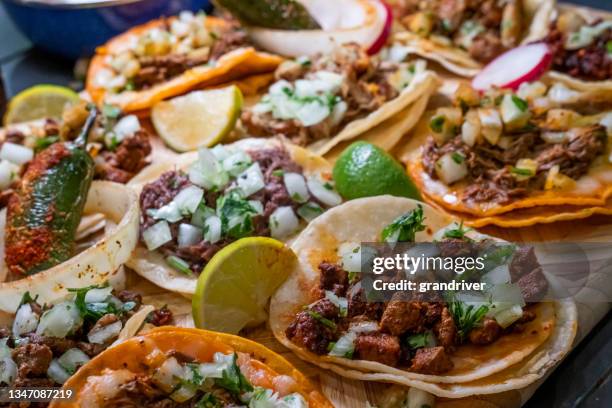 surtido de deliciosos tacos auténticos, birria, carne asada, adobada, cabeza y chicharone, arreglados con rodajas de lima, cebolla y chile asado - street food fotografías e imágenes de stock