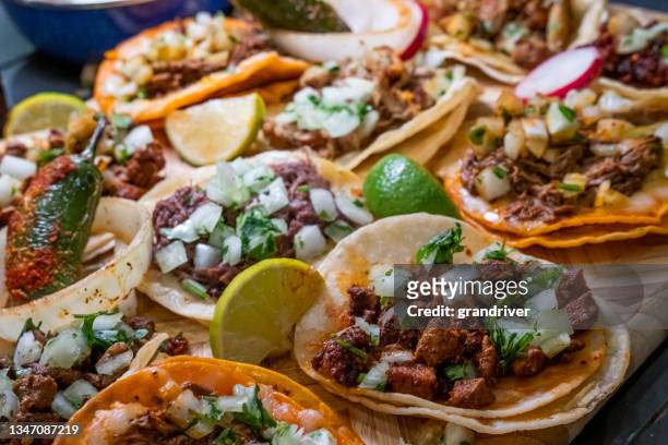 assortment of delicious authentic tacos, birria, carne asada, adobada, cabeza and chicharone, arranged with lime slices, onion, and roasted chili pepper - mexican rustic bildbanksfoton och bilder