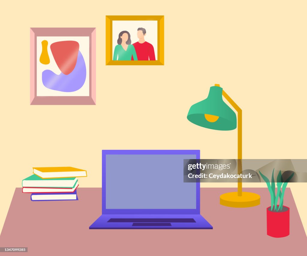 Workspace with laptop , desk lamp, books and plant. Picture frames on the wall