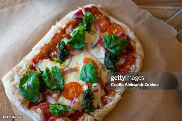 pizza margarita with cheese, ketchup or tomato paste, and basil leaves on a wooden stand or cutting board, on a table in a cafe or fast food restaurant. traditional italian cuisine in a pizzeria. vegetarian food. close-up. - vegetarian pizza stock pictures, royalty-free photos & images