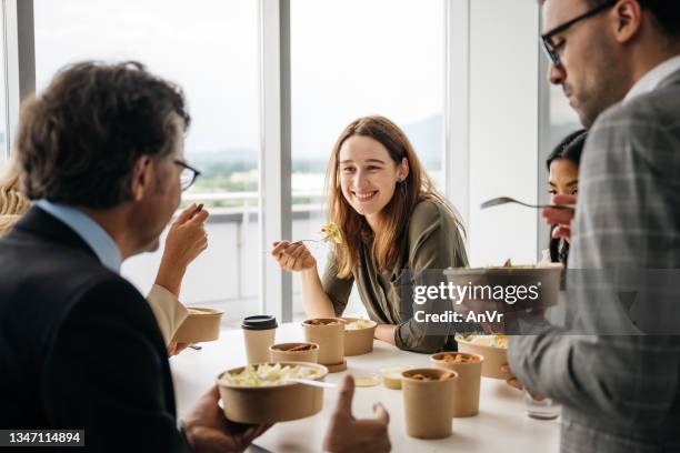 smiling woman enjoying takeaway lunch at work - food to go stockfoto's en -beelden