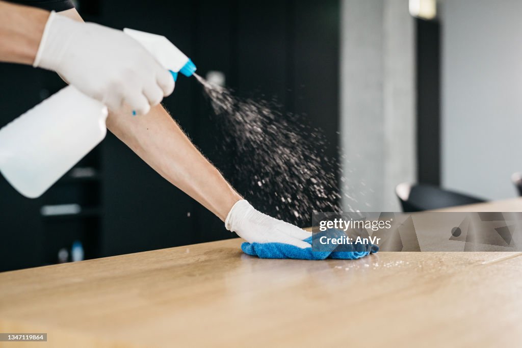 Close-up of disinfecting a wooden desk to limit the spread of COVID-19
