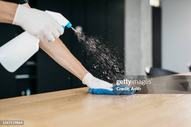 close-up of disinfecting a wooden desk to limit the spread of covid-19 - disinfection stock pictures, royalty-free photos & images