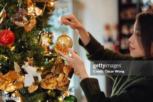 young asian woman decorating christmas tree - hanging christmas lights stock-fotos und bilder