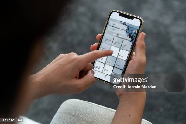teenage boy sitting on sofa and using smart home interface on smartphone - phone hand stock-fotos und bilder