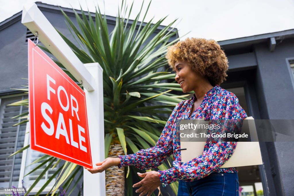 Mature real estate agent adjusting for sale sign in front of home