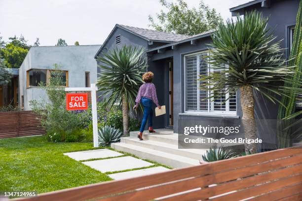 female real estate agent carrying document while walking into house - house with for sale sign stock-fotos und bilder