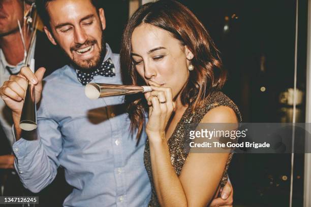 woman with eyes closed blowing party horn while enjoying with male friends at party - party favor foto e immagini stock