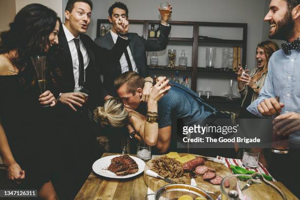 happy male and female friends looking at man kissing girlfriend during party at home - the party inside stock pictures, royalty-free photos & images