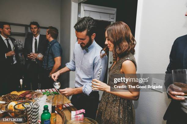 woman talking with male friend making drink while standing at table during party - cocktail party at home stock pictures, royalty-free photos & images