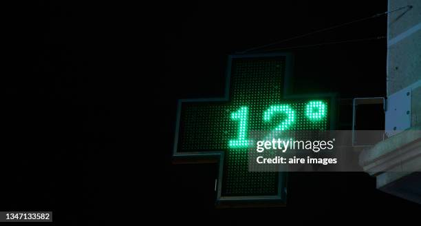 a street side digital thermometer indicating 12 degrees at pharmacy sign - meteorology thermometers stock pictures, royalty-free photos & images