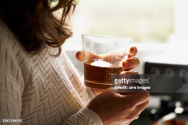 glass cup between hands woman with a glass of whiskey in her hands in front of a window - alcohol and women photos et images de collection