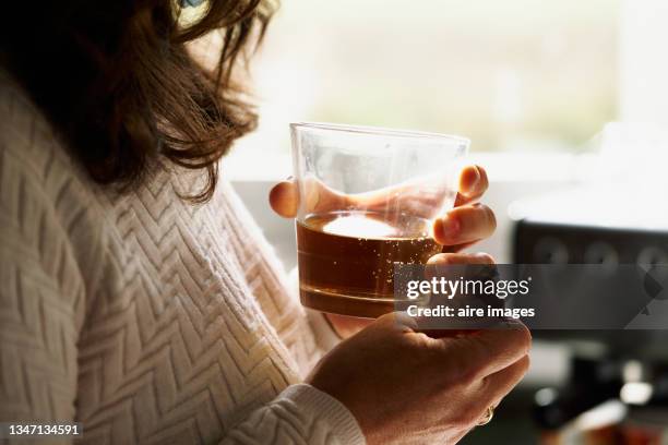 glass cup between hands woman with a glass of whiskey in her hands in front of a window - alcolismo foto e immagini stock