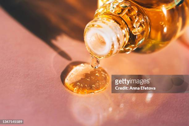 drop of bright yellow essential oil with air bubbles is dripping from glass bottle on pastel pink background. play of shadow and light creates an abstract pattern. trendy colors of the year 2021. extreme close-up - argan oil stock pictures, royalty-free photos & images